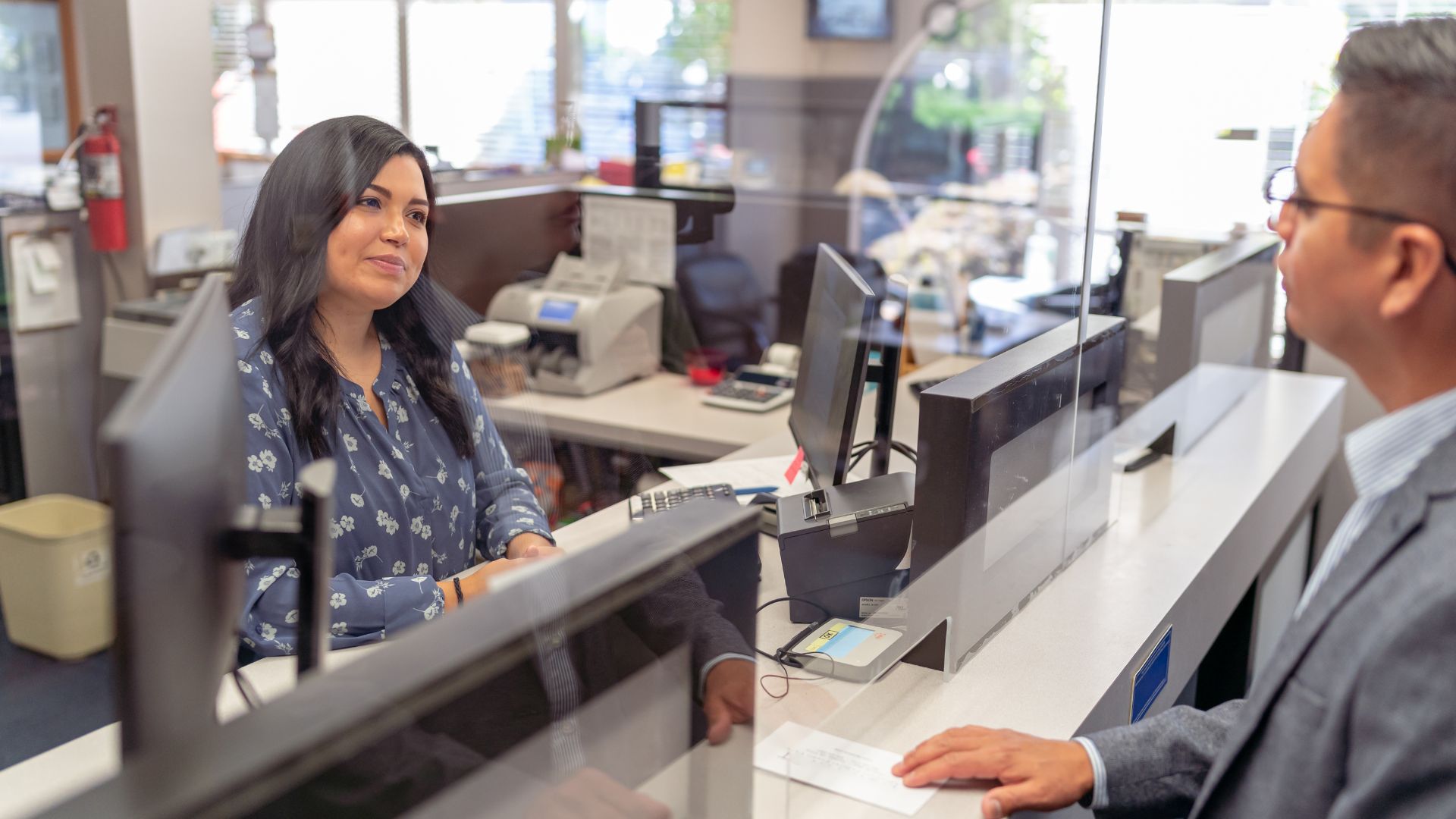 Person interacting with a bank employee at a modern bank branch, demonstrating effective communication with essential English banking phrases.