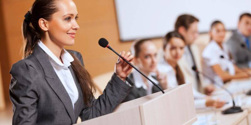 An empowered speaker on stage confidently delivering a speech, their mastery of the American accent evident in their poised delivery, connecting deeply with a diverse and engaged audience, exemplifying the symbiotic relationship between public speaking and confidence.